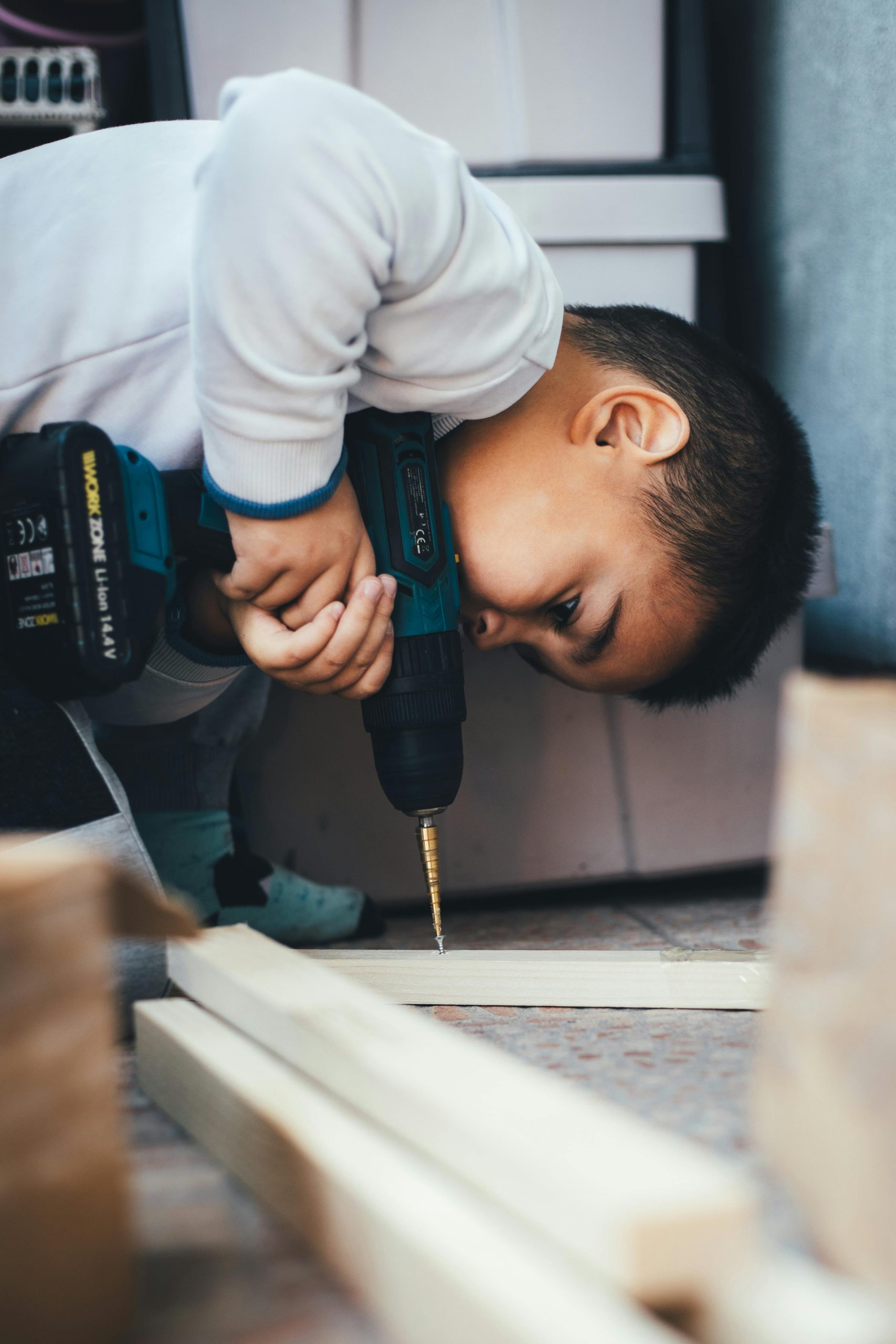 Jeune garçon utilisant une perceuse en intérieur, explorant le travail du bois en toute sécurité et de manière créative.