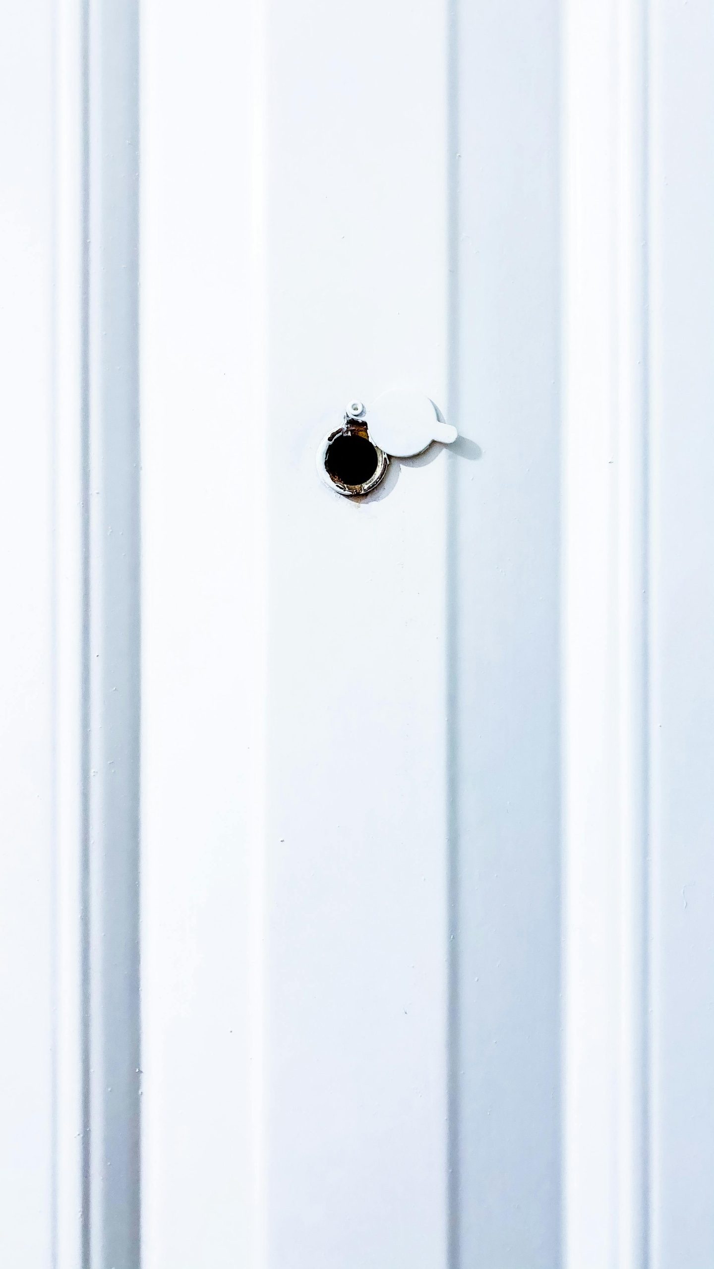 Une simple porte blanche avec un judas muni d'un petit cache, mettant en valeur un design d'intérieur minimaliste.
