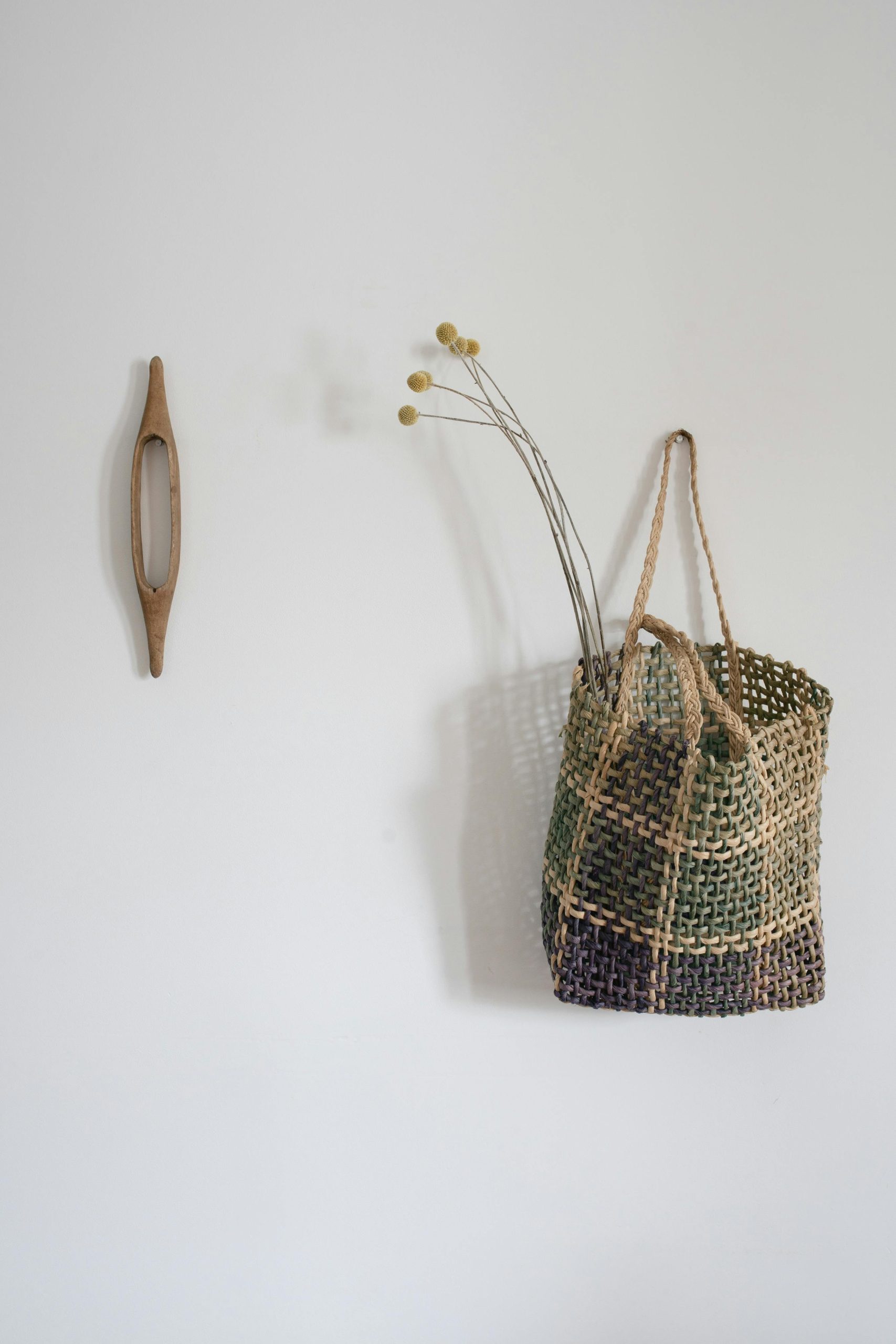 Un sac tissé simple avec des fleurs séchées accroché à un mur blanc minimaliste, ajoutant un charme rustique.