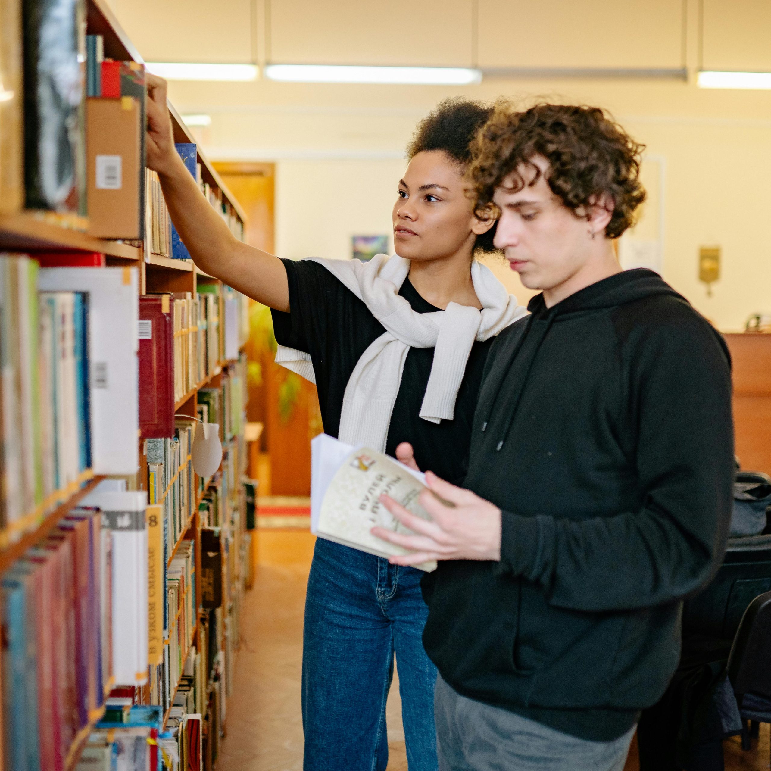 Deux jeunes adultes lisant et faisant des recherches dans une bibliothèque.
