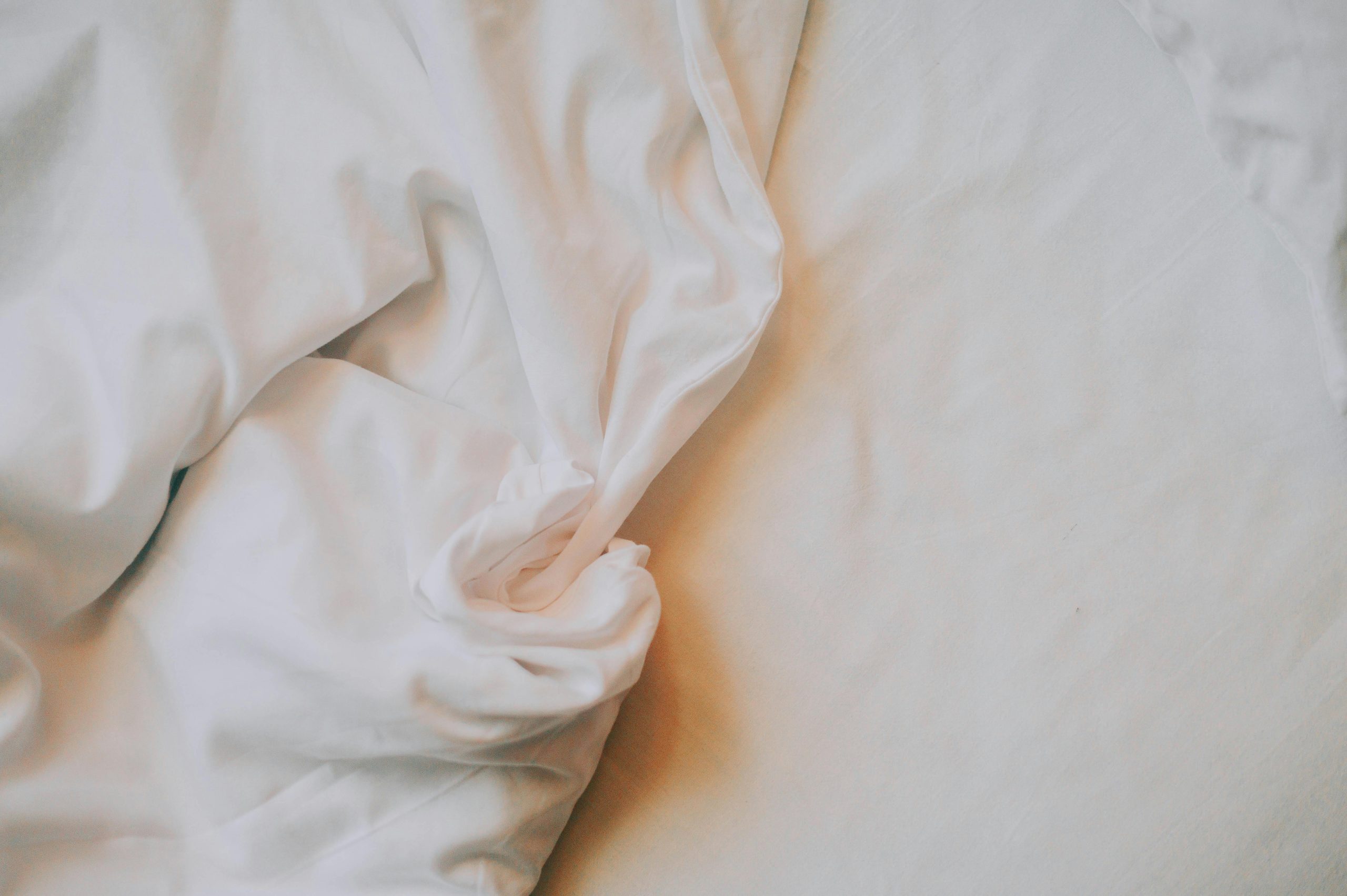 Un gros plan artistique de draps blancs froissés sous un éclairage doux et chaud.