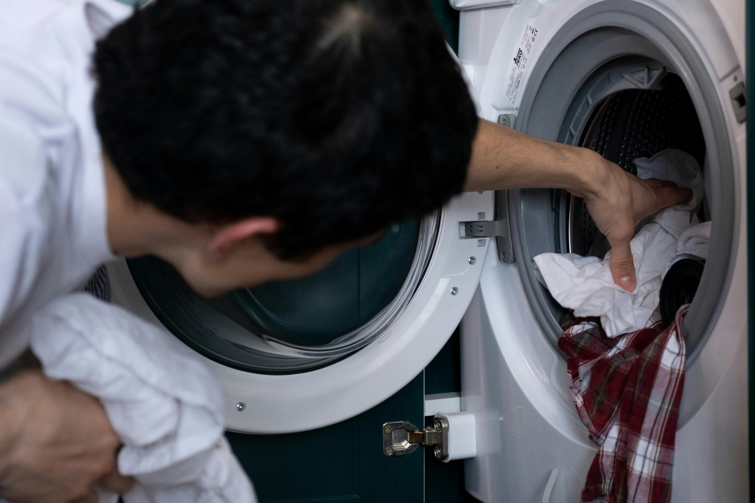Close-up of a man placing clothes into a washing machine during household chores. Gros plan d'un homme plaçant des vêtements dans une machine à laver pendant les tâches ménagères.
