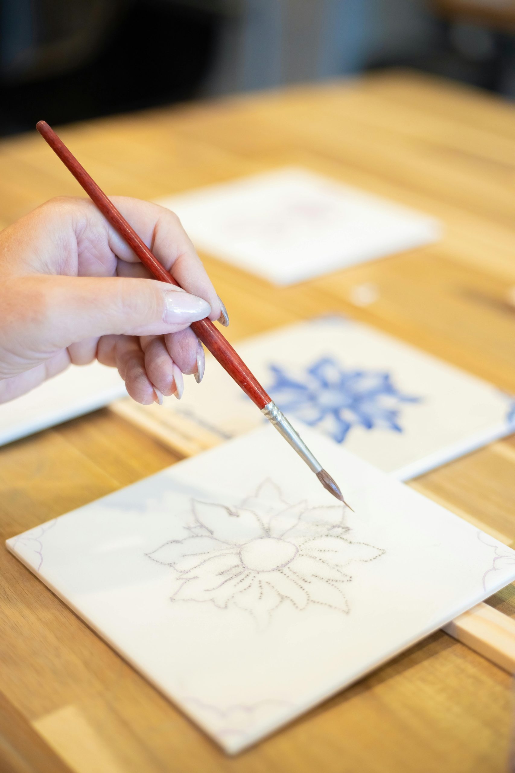 Close-up of hand painting a ceramic tile with floral design in a Portuguese workshop. Gros plan d'une main peignant un carreau de céramique avec un design floral dans un atelier portugais.