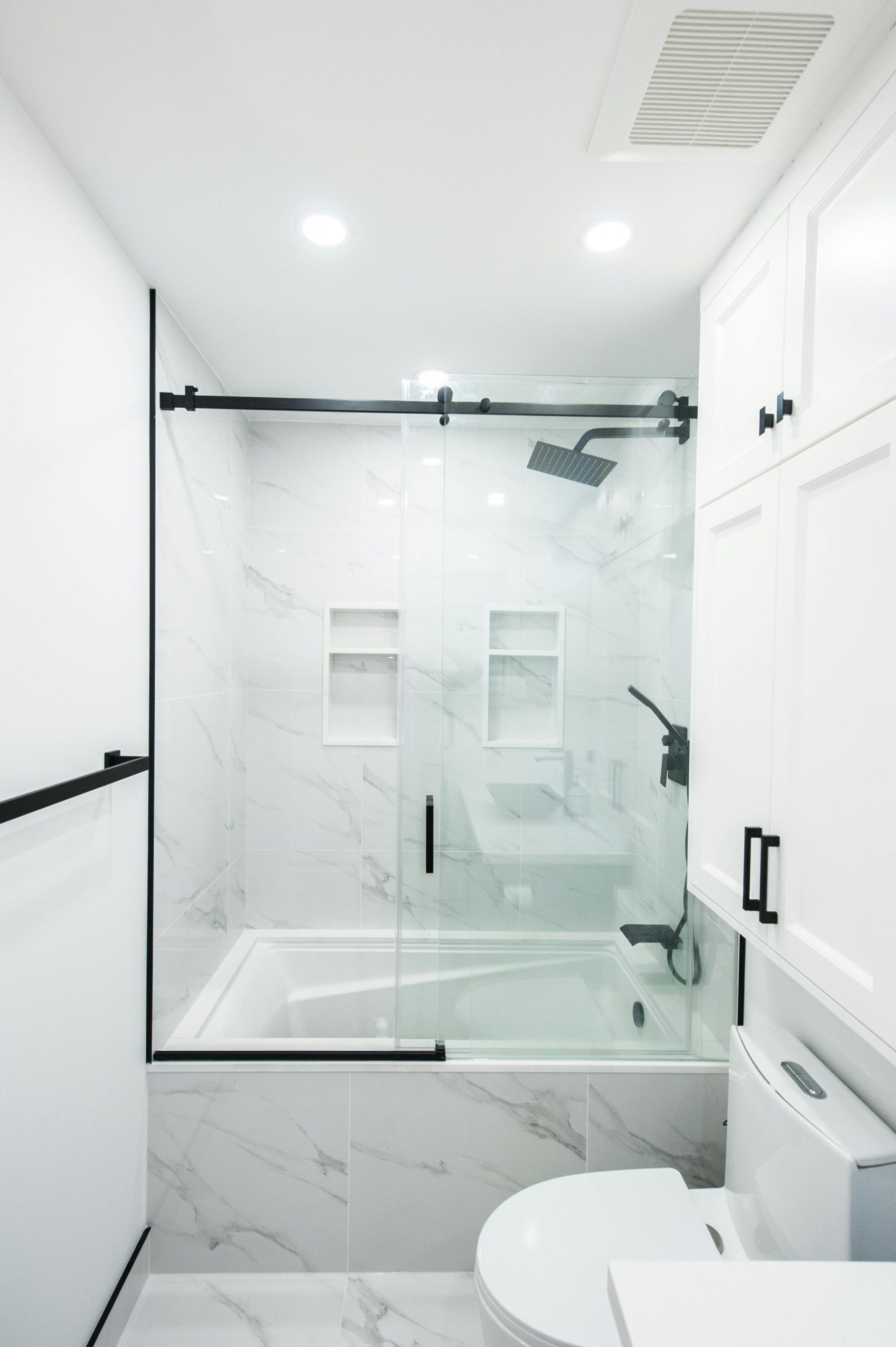 Sleek and modern bathroom featuring white marble tiles, glass shower doors, and black accents. Salle de bain épurée et moderne avec carrelage en marbre blanc, portes de douche en verre et accents noirs.