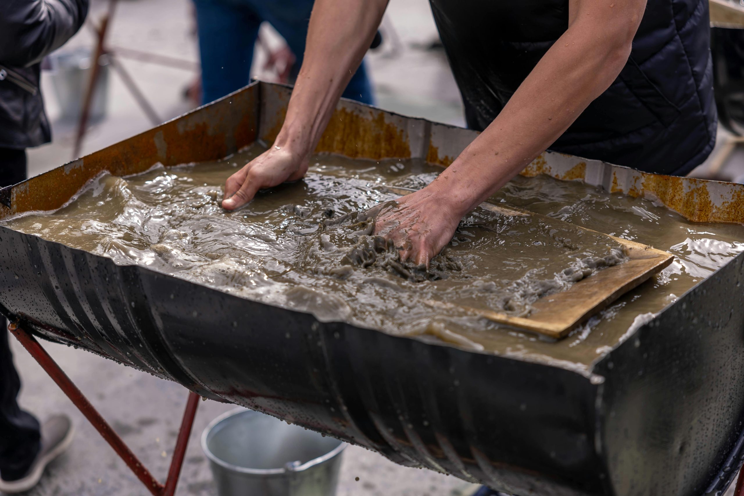 Hands mixing concrete slurry in a large container for construction work outdoors. Des mains mélangeant du mortier de béton dans un grand récipient pour des travaux de construction en extérieur.