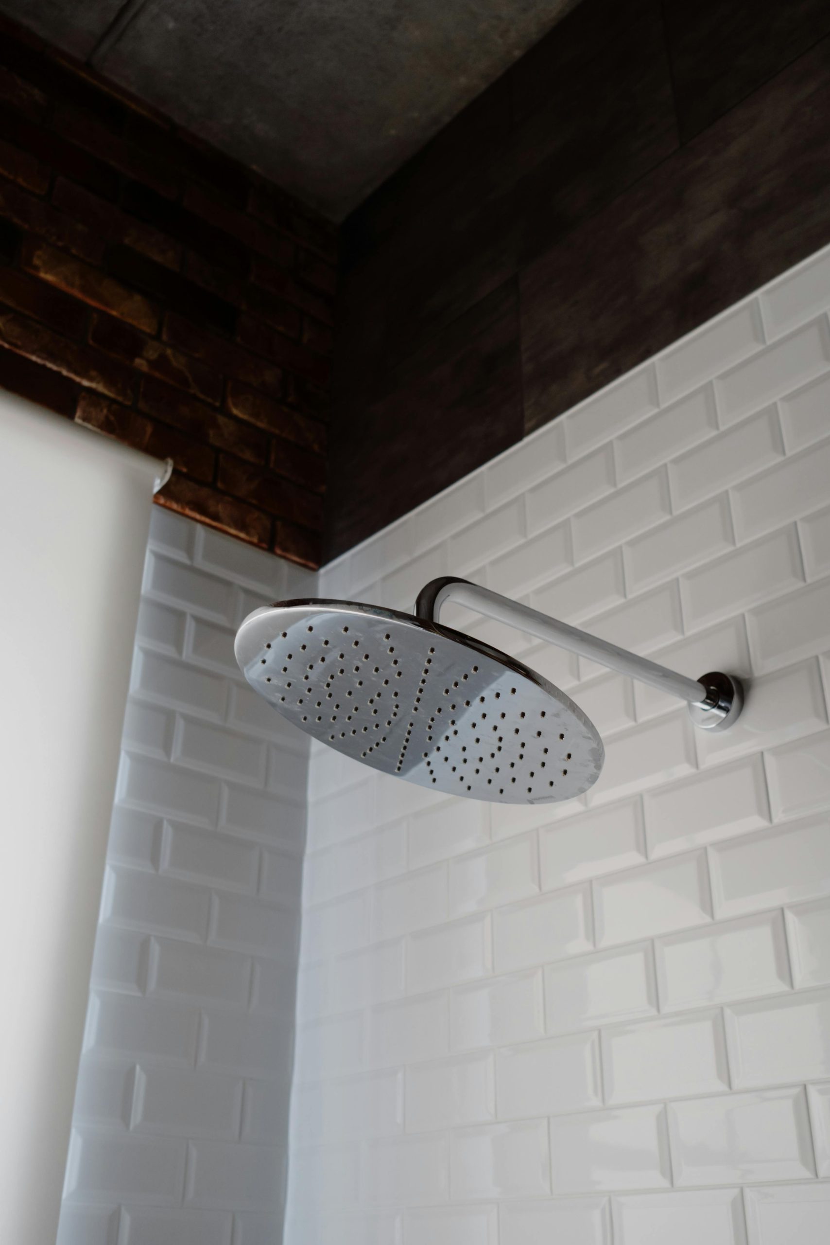 Pomme de douche en acier inoxydable élégante contre une salle de bain stylisée avec des carreaux blancs et un mur d'accent en brique.