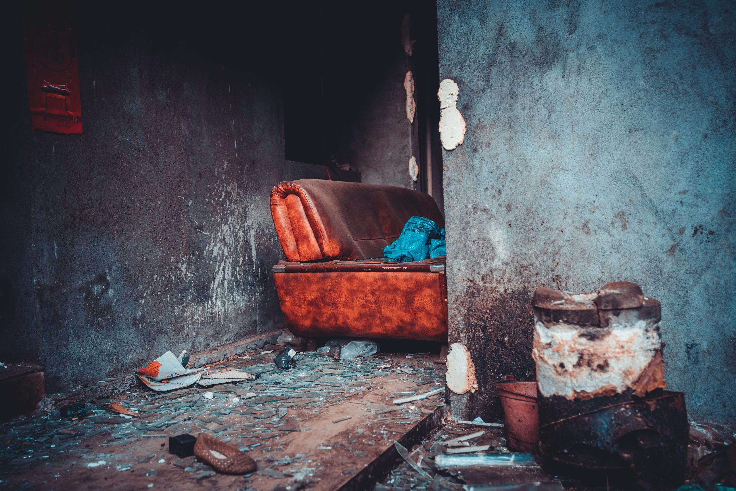 A decaying interior featuring an old leather sofa with debris scattered on the floor. Un intérieur en décadence avec un vieux canapé en cuir et des débris éparpillés sur le sol.