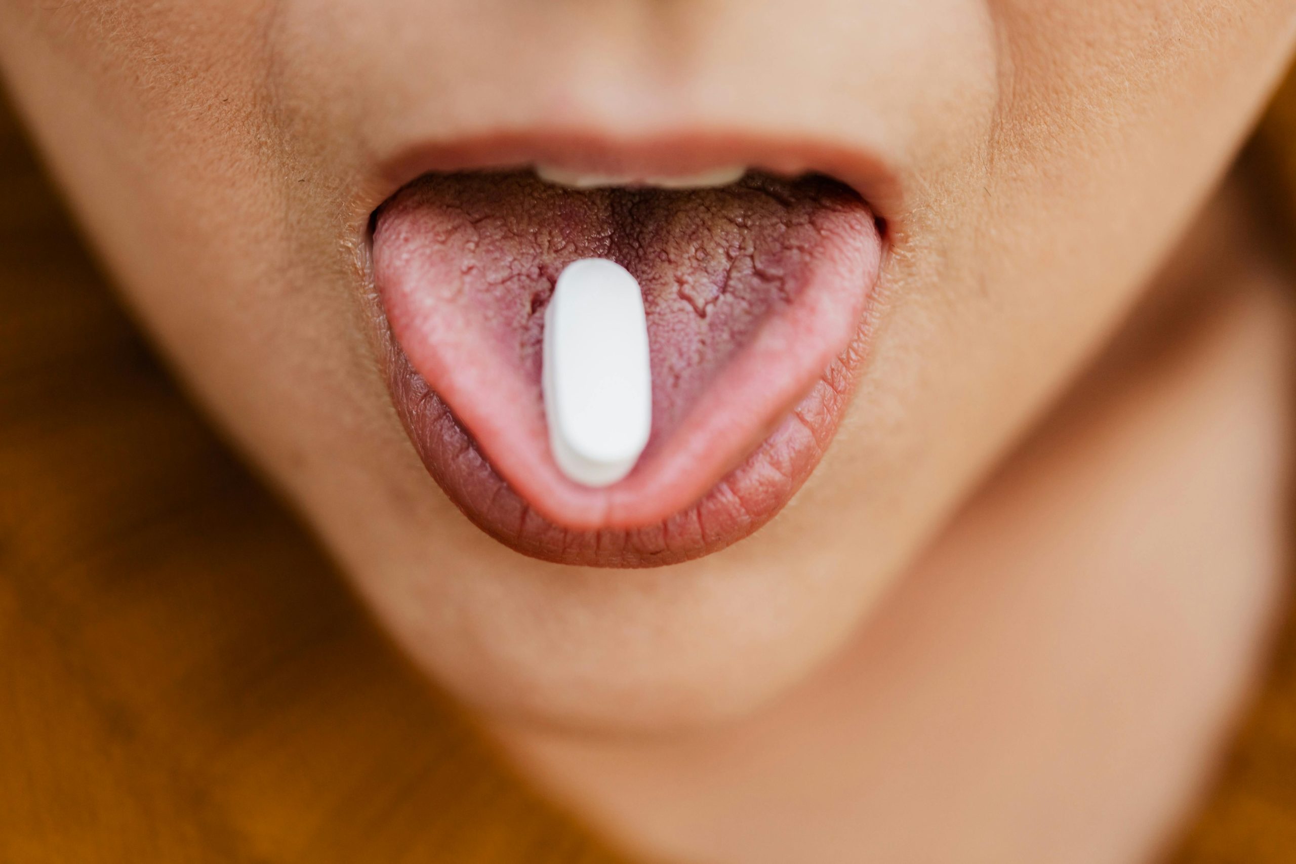 Close-up image of a person placing a pill on their tongue, symbolizing medication or health care. Gros plan d'une personne plaçant un comprimé sur sa langue, symbolisant la médication ou les soins de santé.