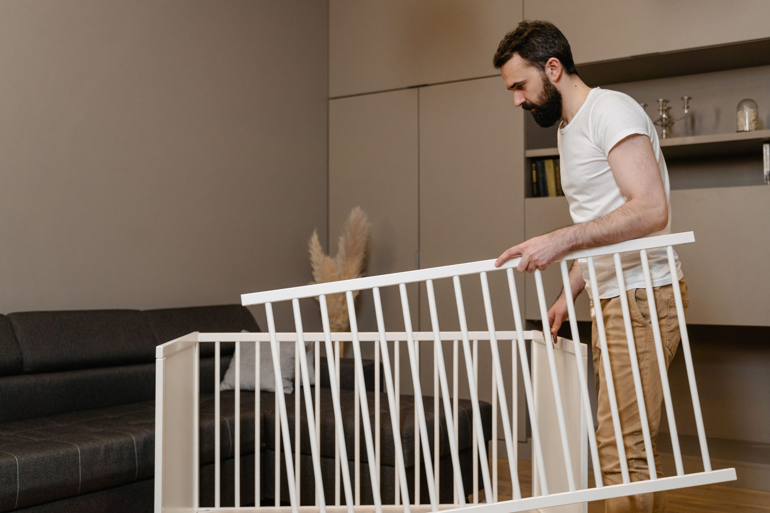 A bearded man assembles a crib in a stylish living room setting. Un homme barbu assemble un berceau dans un salon élégant.