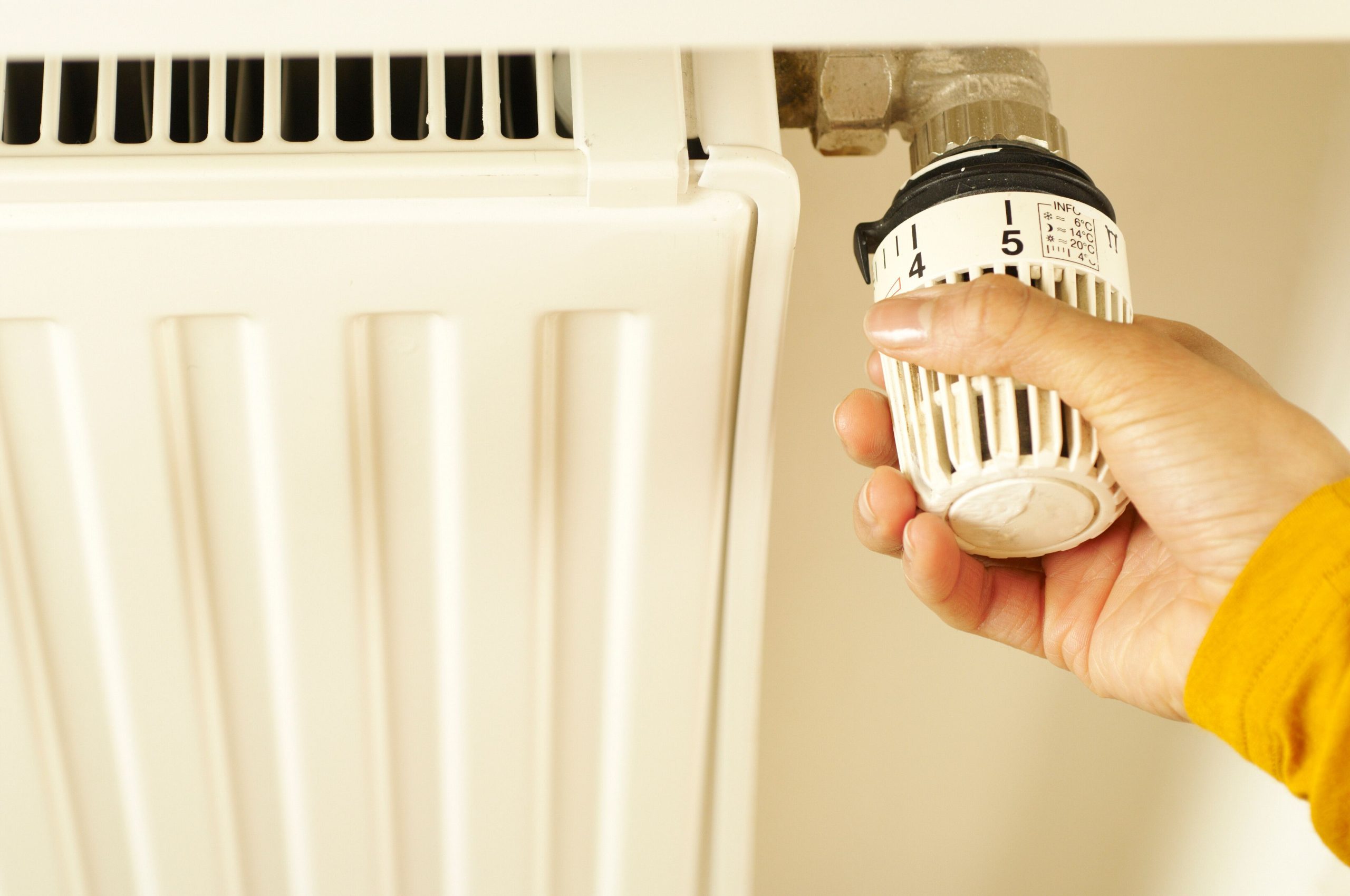 Close-up of hand adjusting radiator thermostat to control home heating temperature. Gros plan sur une main réglant le thermostat du radiateur pour contrôler la température de chauffage de la maison.