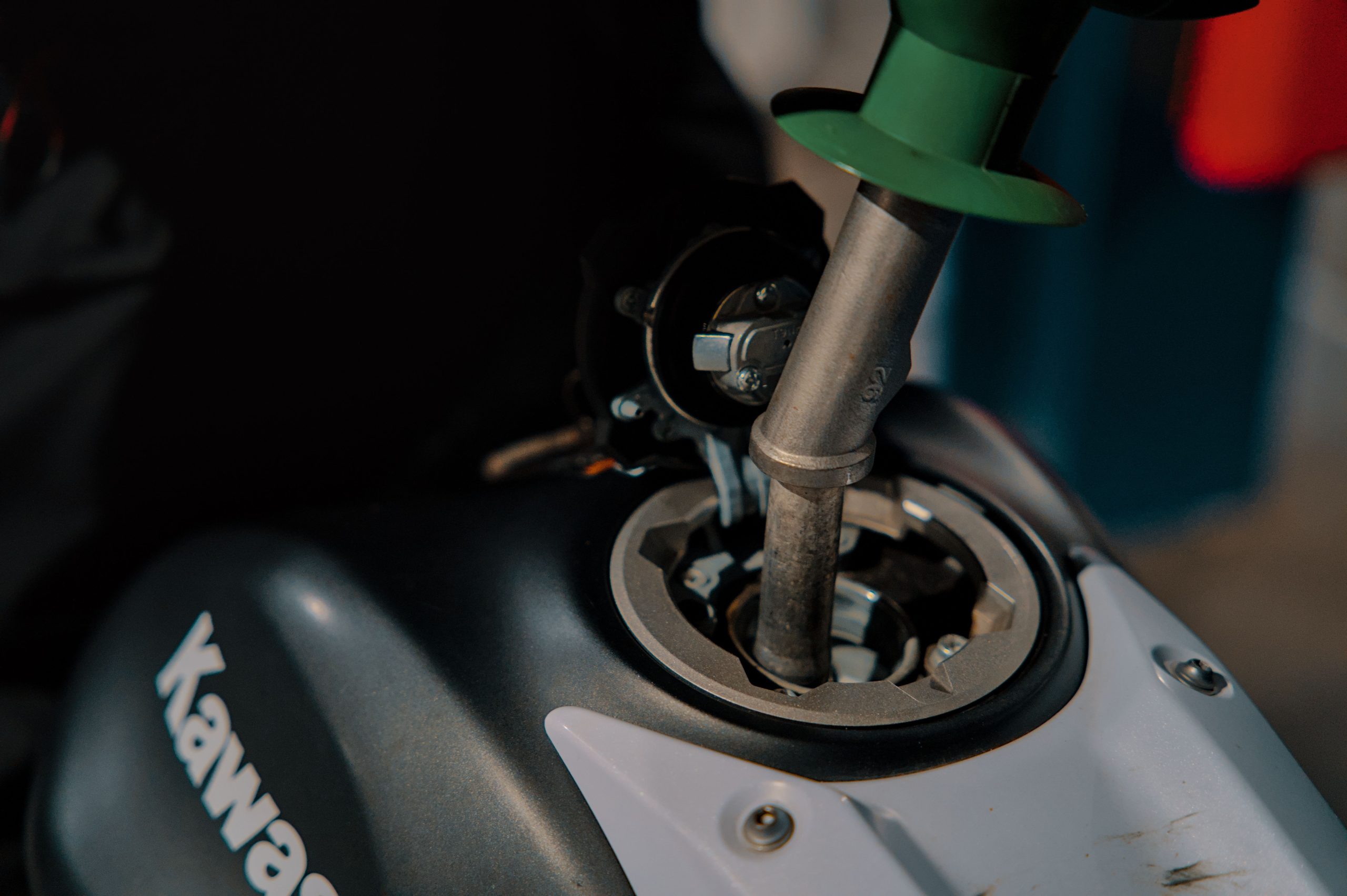 Close-up of refueling a Kawasaki motorcycle at a gas station, with nozzle inserted into the tank. Gros plan sur le ravitaillement en carburant d'une moto Kawasaki à une station-service, avec l'embout inséré dans le réservoir.