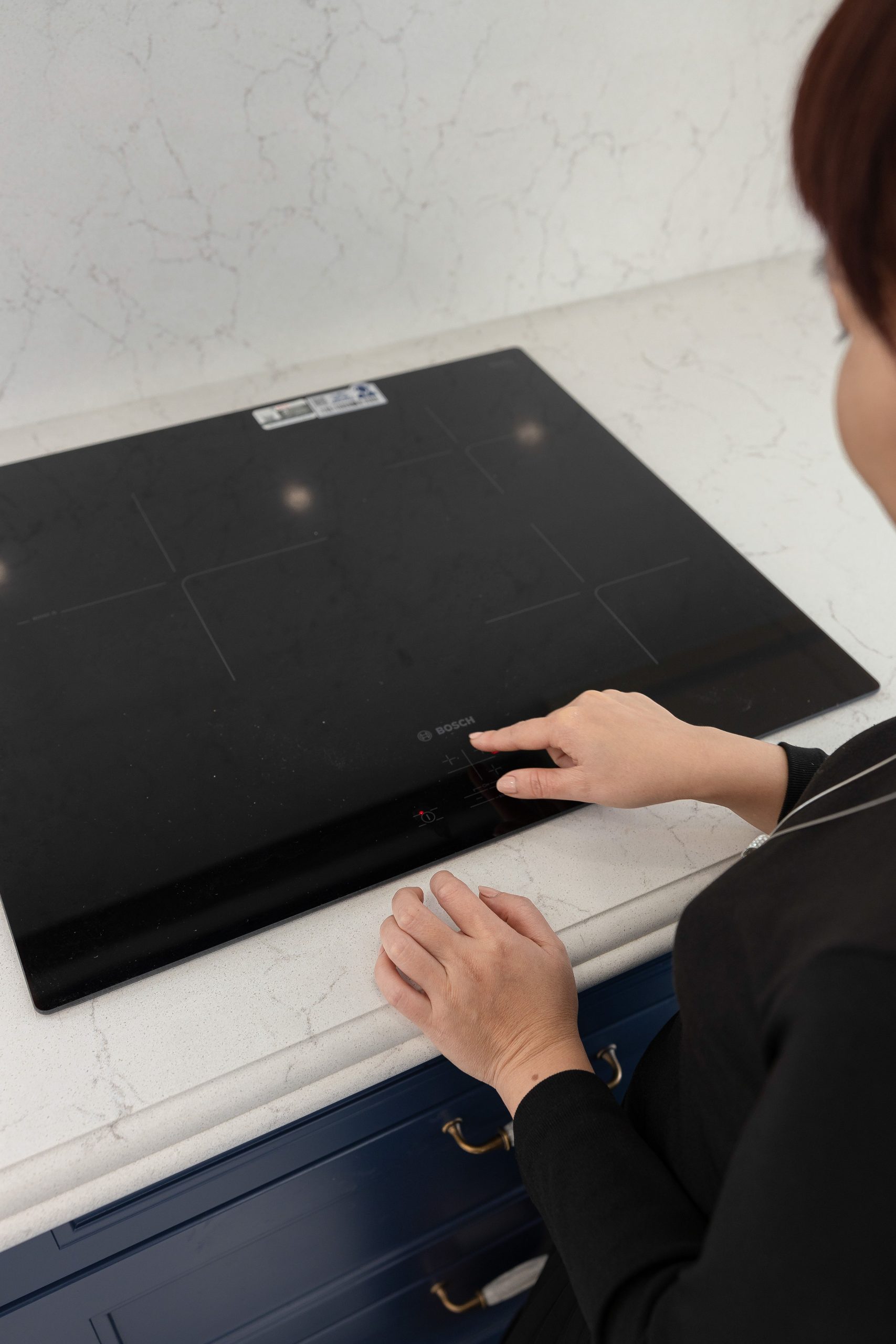 A person interacts with a sleek black induction cooktop in a modern kitchen setting. Une personne interagit avec une cuisinière à induction noire élégante dans un cadre de cuisine moderne.
